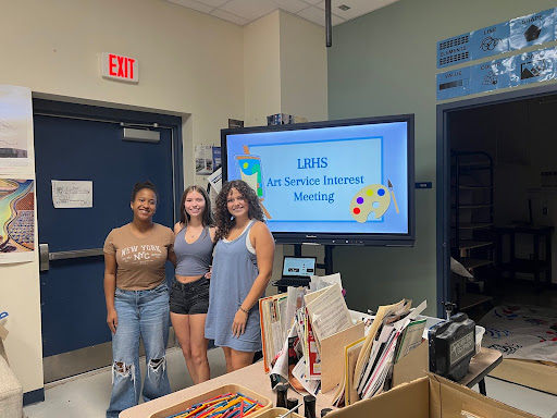 Pictured above: the LRHS Art Service Club officers, Holland Purcell, Keira Dillon, and Katie Carrigan, all seniors, before presenting their interest meeting slide show. They are to be joined in the next meeting by their photographer, Nabila Tabasum, senior. (Photo used by permission of Valentina Fernandez)